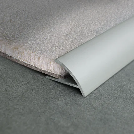 Close-up of a rolled grey carpet with foam padding underlayment on a gray floor surface, showing texture detail and curled edge.