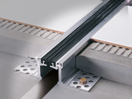 Close-up of a metal floor track and tile edge trim installed between concrete slabs.