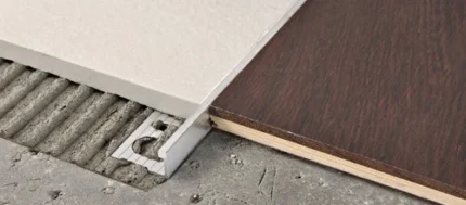 Close-up of a metal floor transition strip being installed between a concrete subfloor and a dark wood laminate plank.