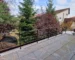 Modern balcony with gray tiled floor and black metal railing overlooking a garden with evergreen trees and shrubs. A black grill is on the left. PROFILITEC picuratoare plinte coltare terminatii profile profesionale